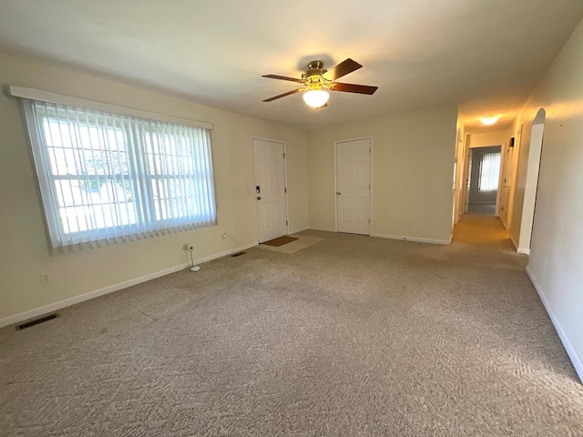 carpeted spare room featuring arched walkways, visible vents, baseboards, and ceiling fan