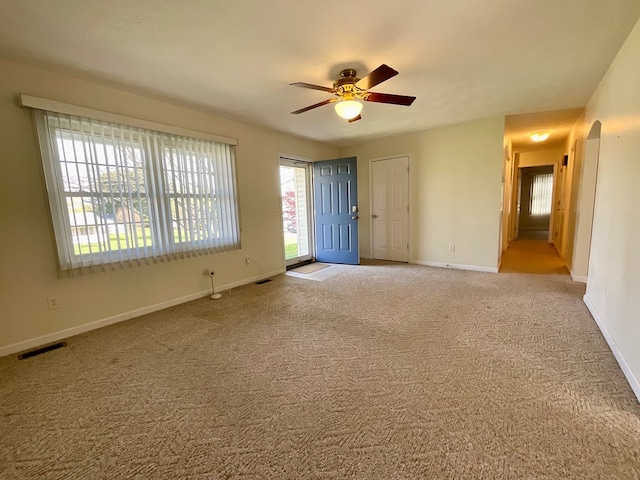 carpeted empty room featuring arched walkways, baseboards, a ceiling fan, and visible vents