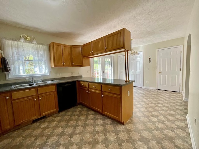 kitchen with dark floors, dark countertops, dishwasher, a sink, and brown cabinetry