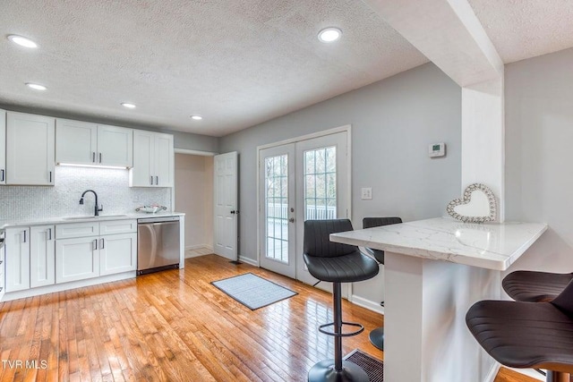 kitchen featuring stainless steel dishwasher, a sink, a kitchen breakfast bar, a textured ceiling, and light wood-style floors