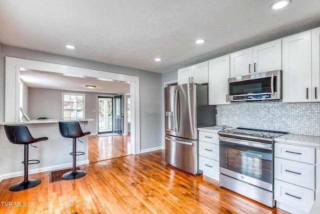 kitchen featuring appliances with stainless steel finishes, a breakfast bar, light countertops, baseboards, and decorative backsplash