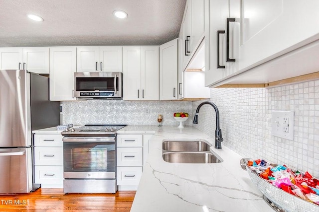 kitchen featuring stainless steel appliances, a sink, white cabinets, light stone counters, and decorative backsplash