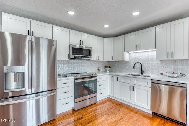 kitchen featuring stainless steel appliances, a sink, white cabinets, tasteful backsplash, and recessed lighting