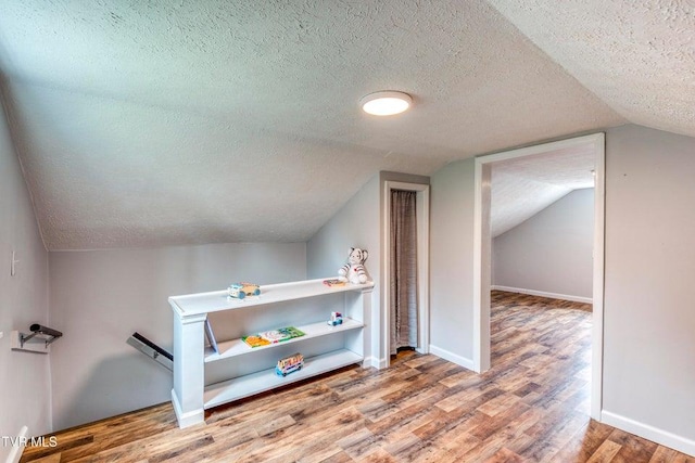 additional living space with a textured ceiling, wood finished floors, lofted ceiling, and baseboards