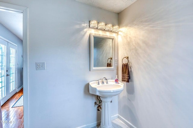 bathroom with baseboards, wood finished floors, a textured ceiling, and french doors