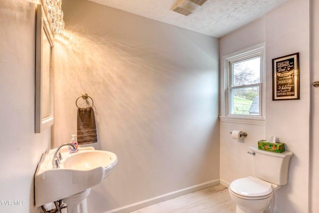 bathroom featuring toilet, a textured ceiling, baseboards, a sink, and wood finished floors