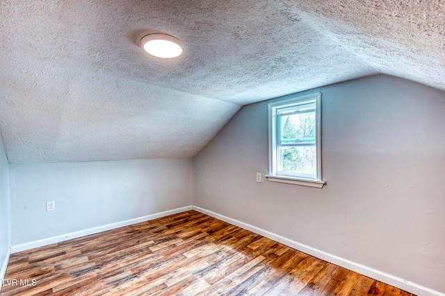 additional living space with a textured ceiling, baseboards, wood finished floors, and vaulted ceiling