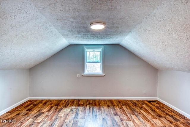 additional living space featuring a textured ceiling, baseboards, hardwood / wood-style floors, and vaulted ceiling