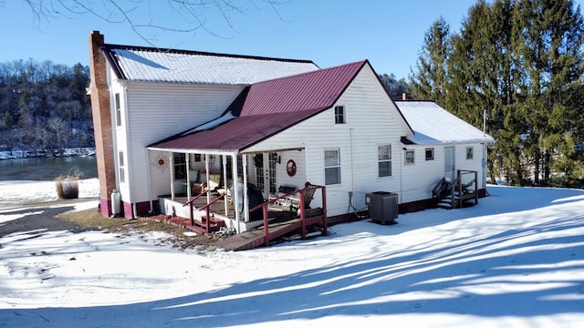 snow covered house featuring central AC, metal roof, and a chimney