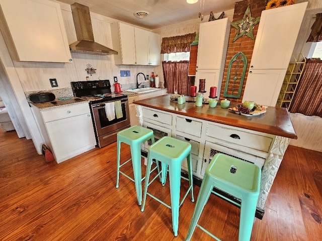 kitchen with electric range, wood finished floors, a sink, white cabinetry, and wall chimney range hood