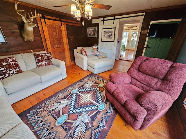 living room featuring a barn door, wooden walls, ceiling fan, wood finished floors, and crown molding