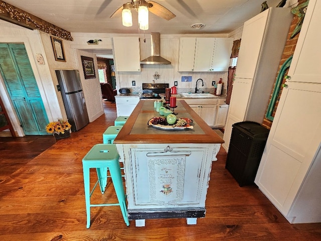 kitchen with wall chimney exhaust hood, appliances with stainless steel finishes, dark wood-type flooring, white cabinetry, and a sink