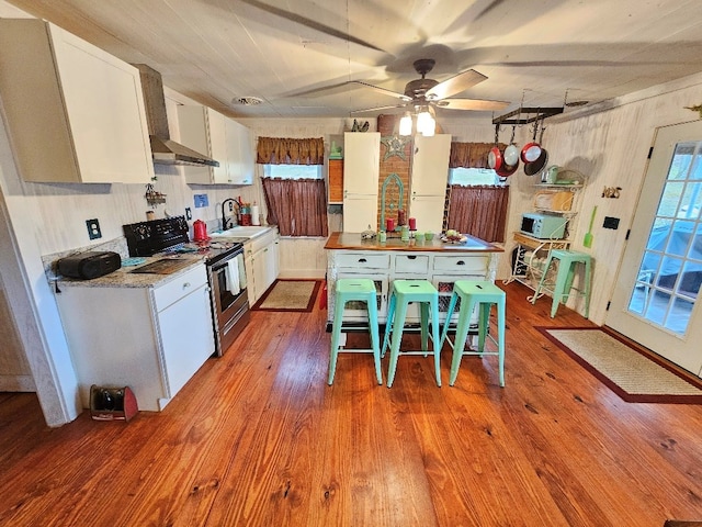 kitchen with white microwave, electric range, a sink, white cabinetry, and wood-type flooring