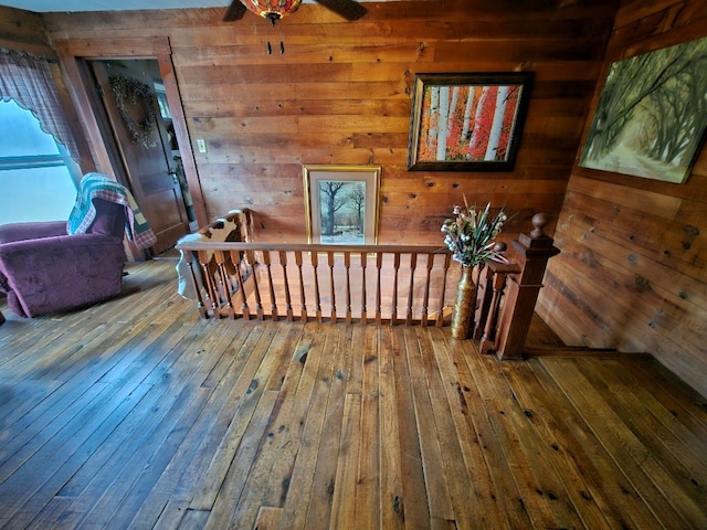 hall featuring wood walls, wood-type flooring, and an upstairs landing