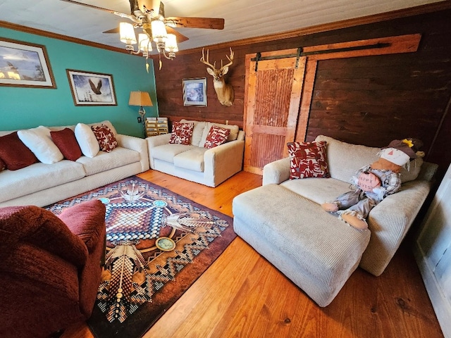 living area with a barn door, wood walls, wood finished floors, a ceiling fan, and crown molding