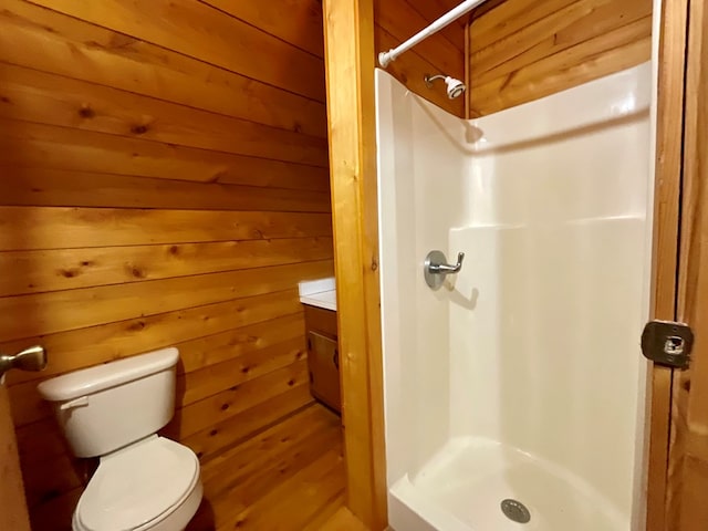 full bathroom featuring wooden walls, a stall shower, toilet, and vanity