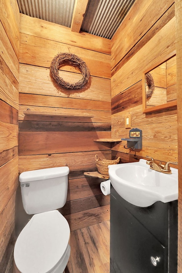 bathroom with toilet, vanity, and wood walls