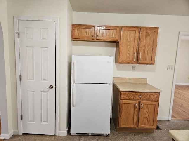 kitchen with brown cabinetry, baseboards, light countertops, and freestanding refrigerator