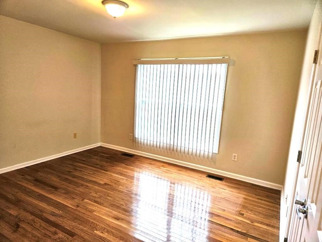 spare room with dark wood-type flooring, visible vents, and baseboards