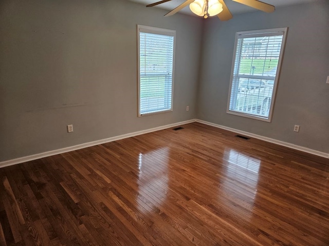 spare room with a ceiling fan, dark wood-style flooring, visible vents, and baseboards