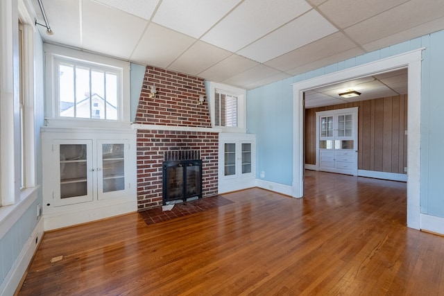 unfurnished living room featuring wooden walls, a paneled ceiling, a fireplace, and hardwood / wood-style floors