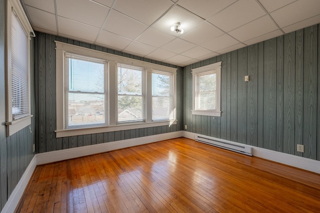 spare room featuring a baseboard heating unit, hardwood / wood-style floors, a drop ceiling, and wood walls