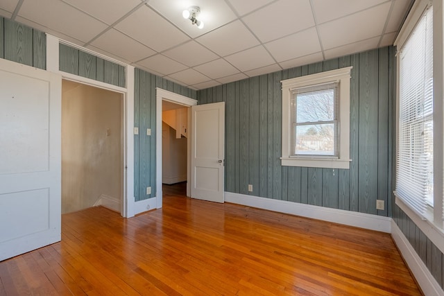 unfurnished room featuring a drop ceiling, hardwood / wood-style floors, and wood walls