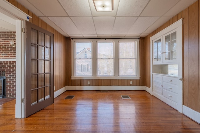 interior space featuring a wood stove, hardwood / wood-style floors, a drop ceiling, and wood walls