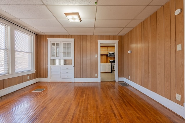 unfurnished living room with wood walls, a drop ceiling, and light hardwood / wood-style flooring