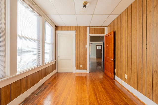 spare room with hardwood / wood-style flooring, wooden walls, and a drop ceiling