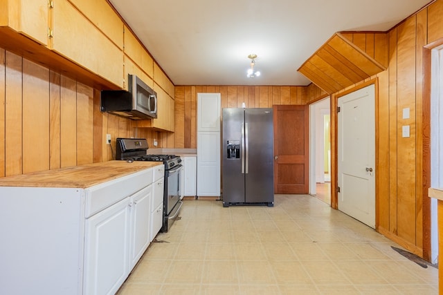 kitchen featuring appliances with stainless steel finishes, wooden walls, and white cabinets