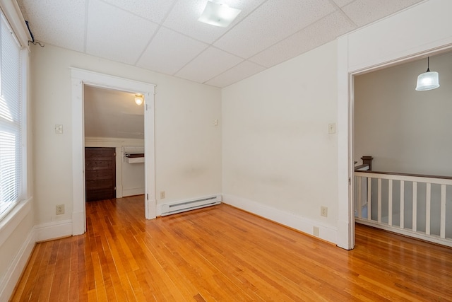 empty room featuring baseboard heating, a paneled ceiling, and wood-type flooring