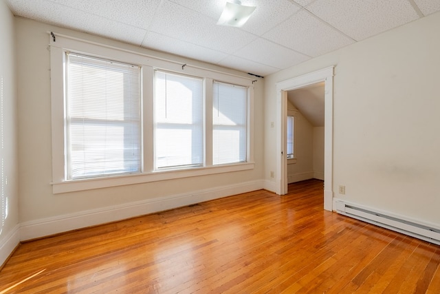 empty room featuring a paneled ceiling, light hardwood / wood-style flooring, and a baseboard heating unit