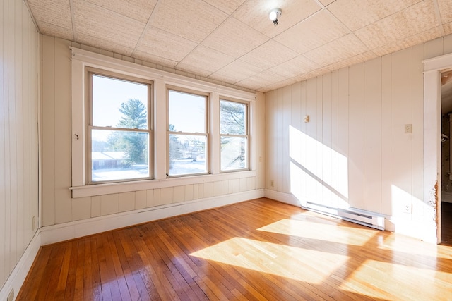 empty room with wood walls, light hardwood / wood-style floors, and a baseboard heating unit