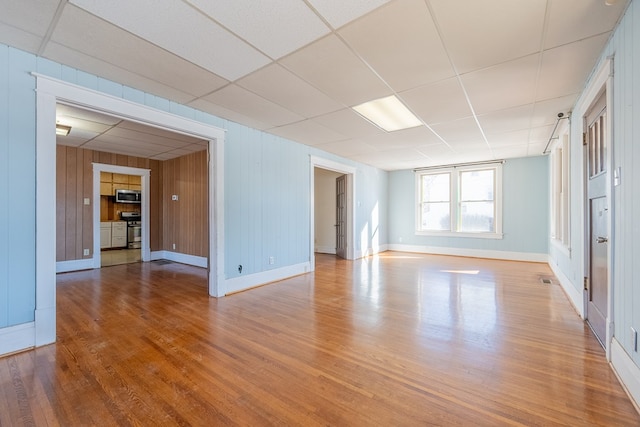 spare room featuring a paneled ceiling, light wood-type flooring, and wood walls