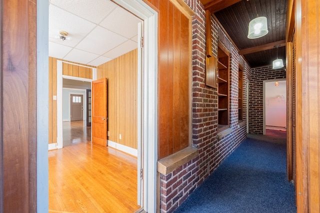 corridor featuring built in features, brick wall, a drop ceiling, and wood walls