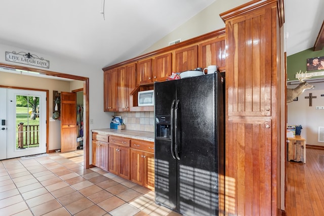 3003 Freestone Valley Rd, Tannersville, VA 24377 - kitchen with black fridge, lofted ceiling, decorative backsplash, brown cabinets, and white microwave