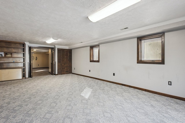 below grade area with a textured ceiling, carpet flooring, visible vents, baseboards, and crown molding