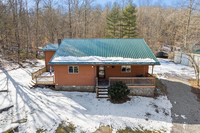 view of front of property featuring covered porch, a chimney, metal roof, and a view of trees