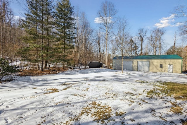 yard covered in snow featuring a garage and an outbuilding