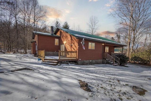 snow covered property featuring metal roof, a chimney, and a wooden deck