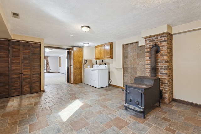 laundry area with cabinet space, a wood stove, stone finish floor, washer and dryer, and baseboards