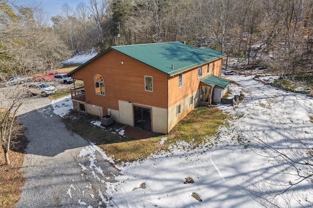 view of snowy exterior featuring metal roof and driveway