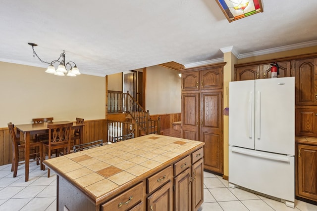 kitchen featuring wooden walls, tile counters, wainscoting, freestanding refrigerator, and a chandelier