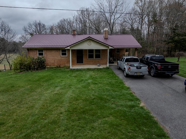 ranch-style home featuring a chimney, metal roof, a front yard, brick siding, and aphalt driveway