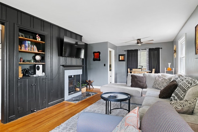 living area with ceiling fan, a large fireplace, baseboards, and light wood-style floors