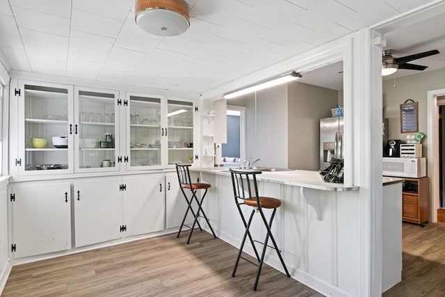 interior space with ceiling fan, white microwave, a sink, light wood-style floors, and stainless steel fridge with ice dispenser