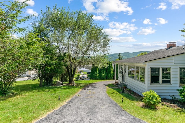 view of property exterior with driveway, a yard, a shingled roof, and a mountain view