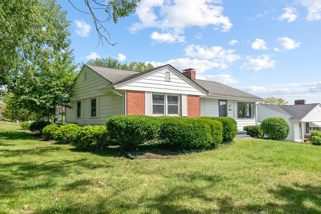 view of front of home with brick siding, a chimney, and a front yard