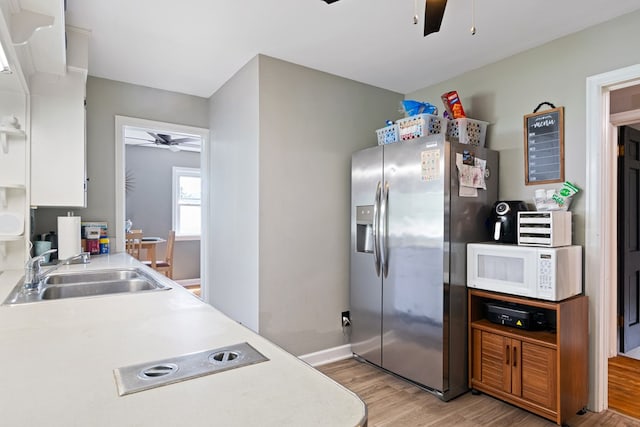 kitchen with ceiling fan, white microwave, a sink, light wood finished floors, and stainless steel fridge